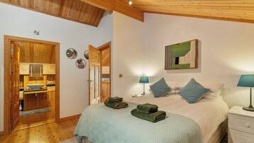 A bedroom with a bed, two bedside lamps, a wooden wardrobe, and a bathroom with a sink and mirror.