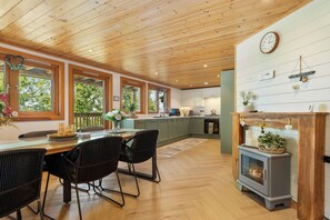 A spacious kitchen with wooden beams, a dining area with chairs, and a fireplace. - The Rowan - Luxury Lodge and Woodland Views (Penally)