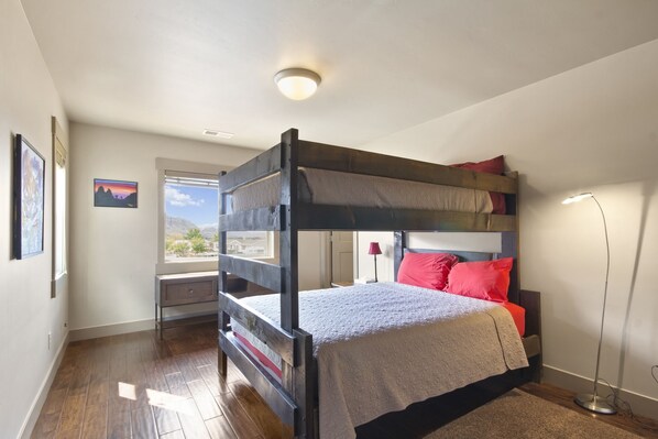 A bunk bed with a desk and chair, a window with a view, and a floor lamp.