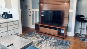 A modern living room with a flat-screen TV, wooden entertainment unit, a coffee table, and a bar stool. - Heavenly Beach-front Apartment in Venice (Los Angeles)