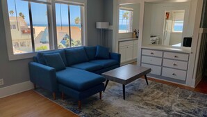 A living room with a blue sectional sofa, a coffee table, and a view of the beach through large windows. - Heavenly Beach-front Apartment in Venice (Los Angeles)