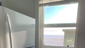A compact kitchen with a white refrigerator, a window with a view of the sea, and a trash bin. - Heavenly Beach-front Apartment in Venice (Los Angeles)
