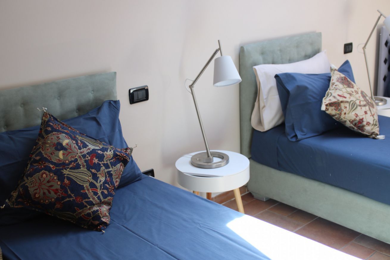 Ett sovrum med två sängar, var och en med ett blått överkast och kuddar, ett sängbord med en lampa och en väggmonterad strömbrytare.