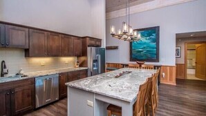 A modern kitchen with dark wooden cabinets, stainless steel appliances, a marble countertop island, and a large painting above the island.