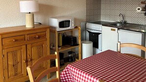 A compact kitchen with wooden cabinets, a microwave, a coffee maker, and a checkered tablecloth. - Appartement F2 Avec Large Balcon (Embrun)
