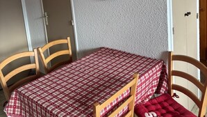 A dining area with a wooden table and chairs, a red and white checkered tablecloth, and a wooden wall clock. - Appartement F2 Avec Large Balcon (Embrun)