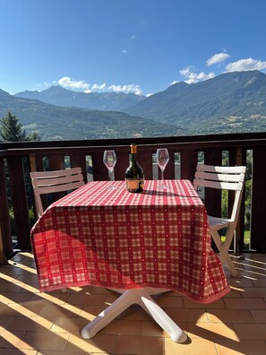 A table with a red and white checkered tablecloth, two wine glasses, and a bottle of wine on a balcony with a mountain view. - Appartement F2 Avec Large Balcon (Embrun)
