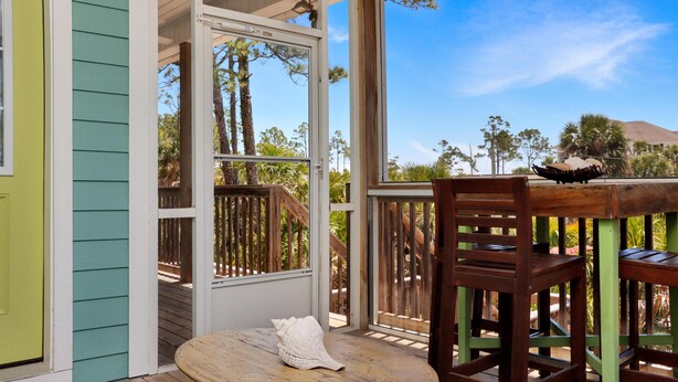 A porch with a wooden table and chairs, a white shell, and a view of trees and a mountain. - Bethany Cottage (Port St. Joe)