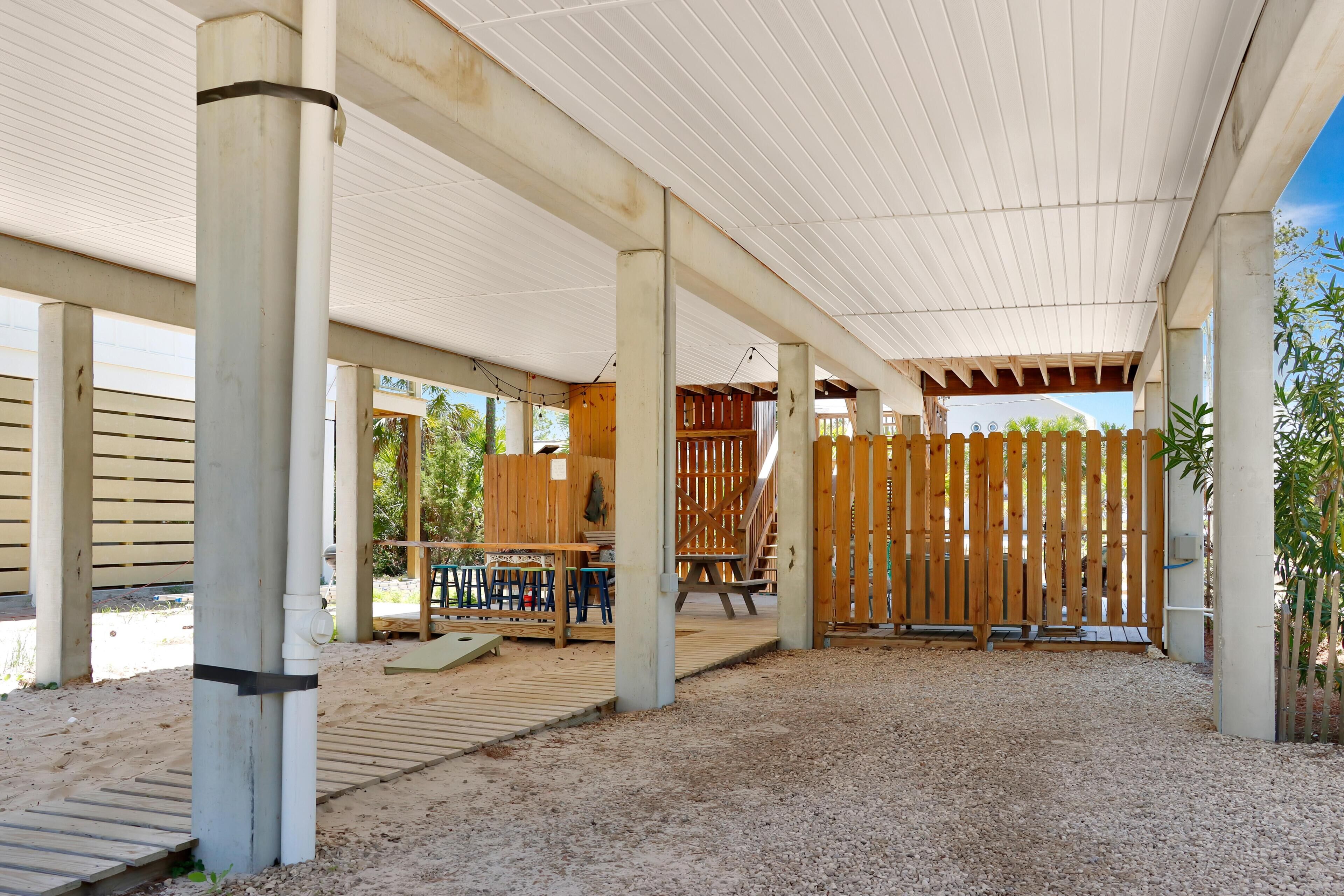 An outdoor covered area with a wooden deck, concrete pillars, and a gravel floor.
