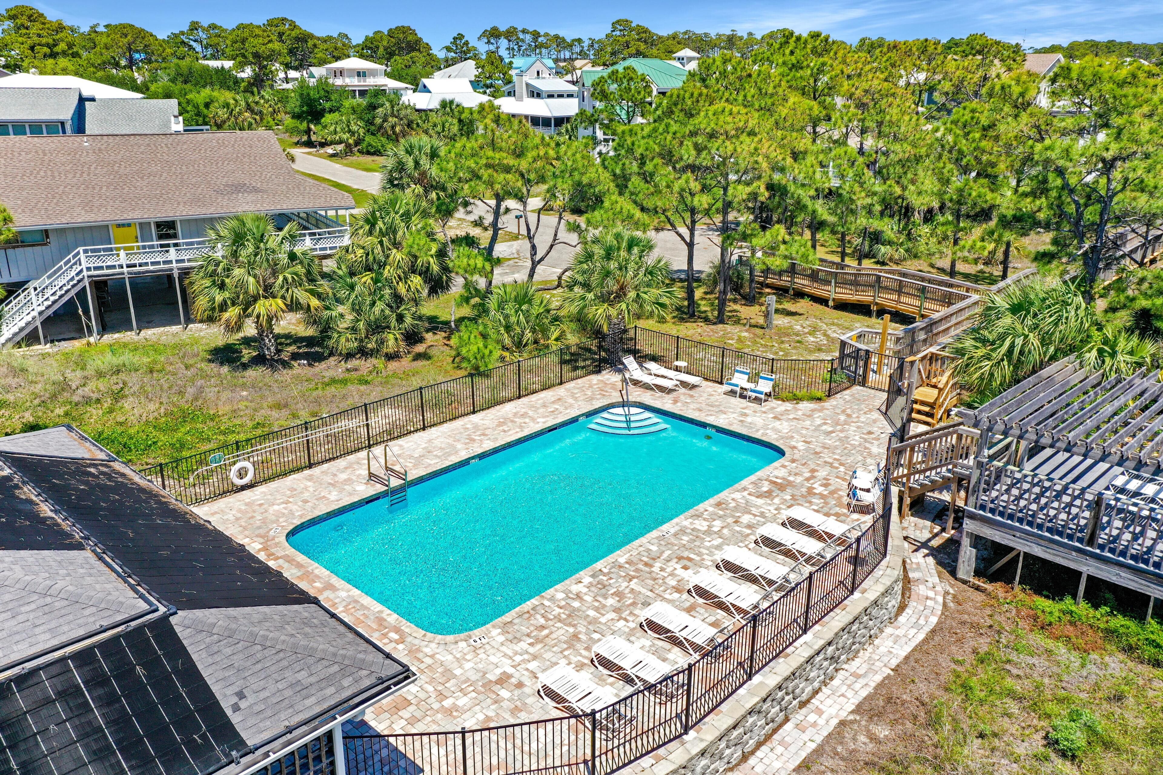 A rectangular swimming pool with a wooden deck and lounge chairs, surrounded by a fence and trees.