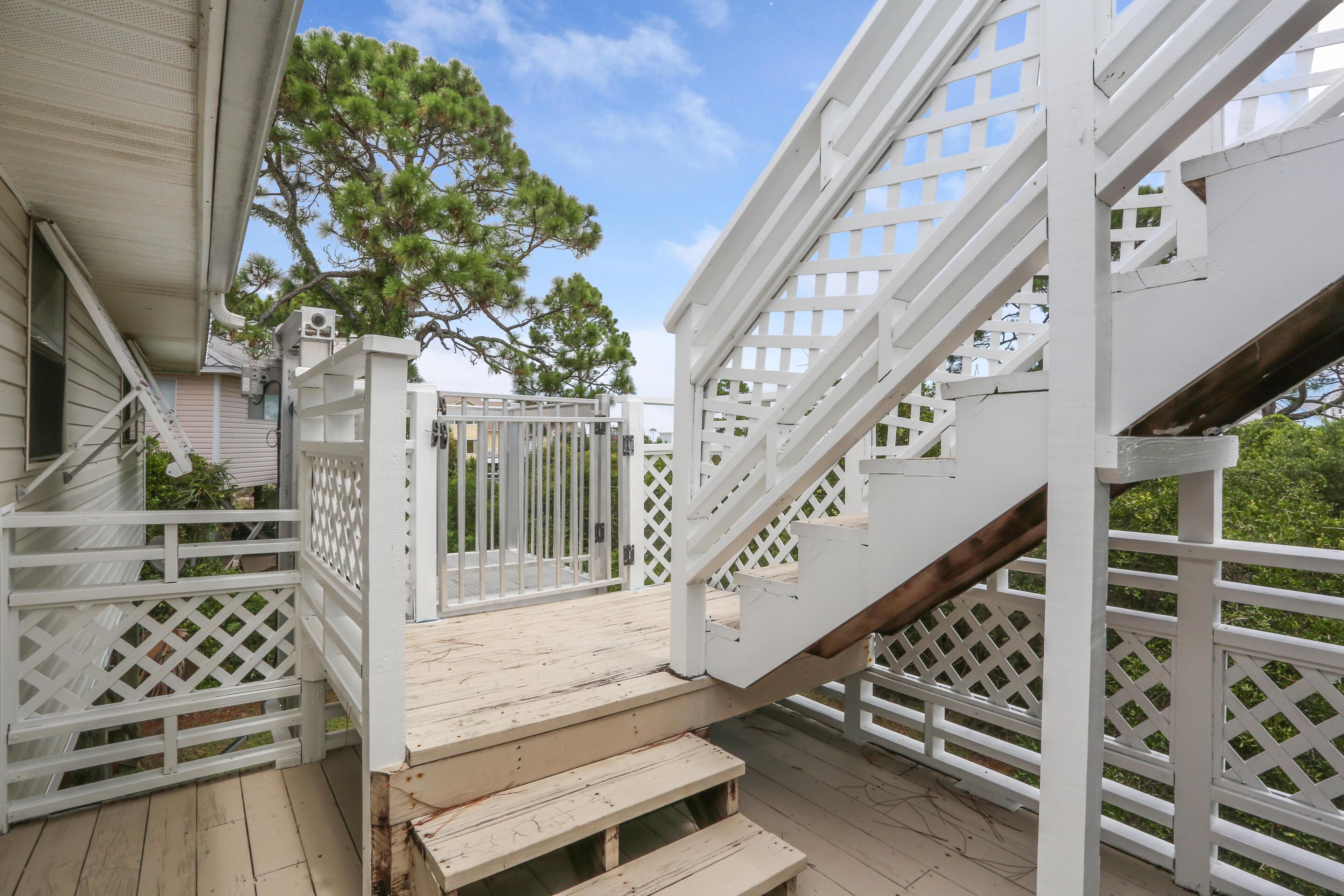 A wooden deck with a white staircase and railings, surrounded by a white fence.