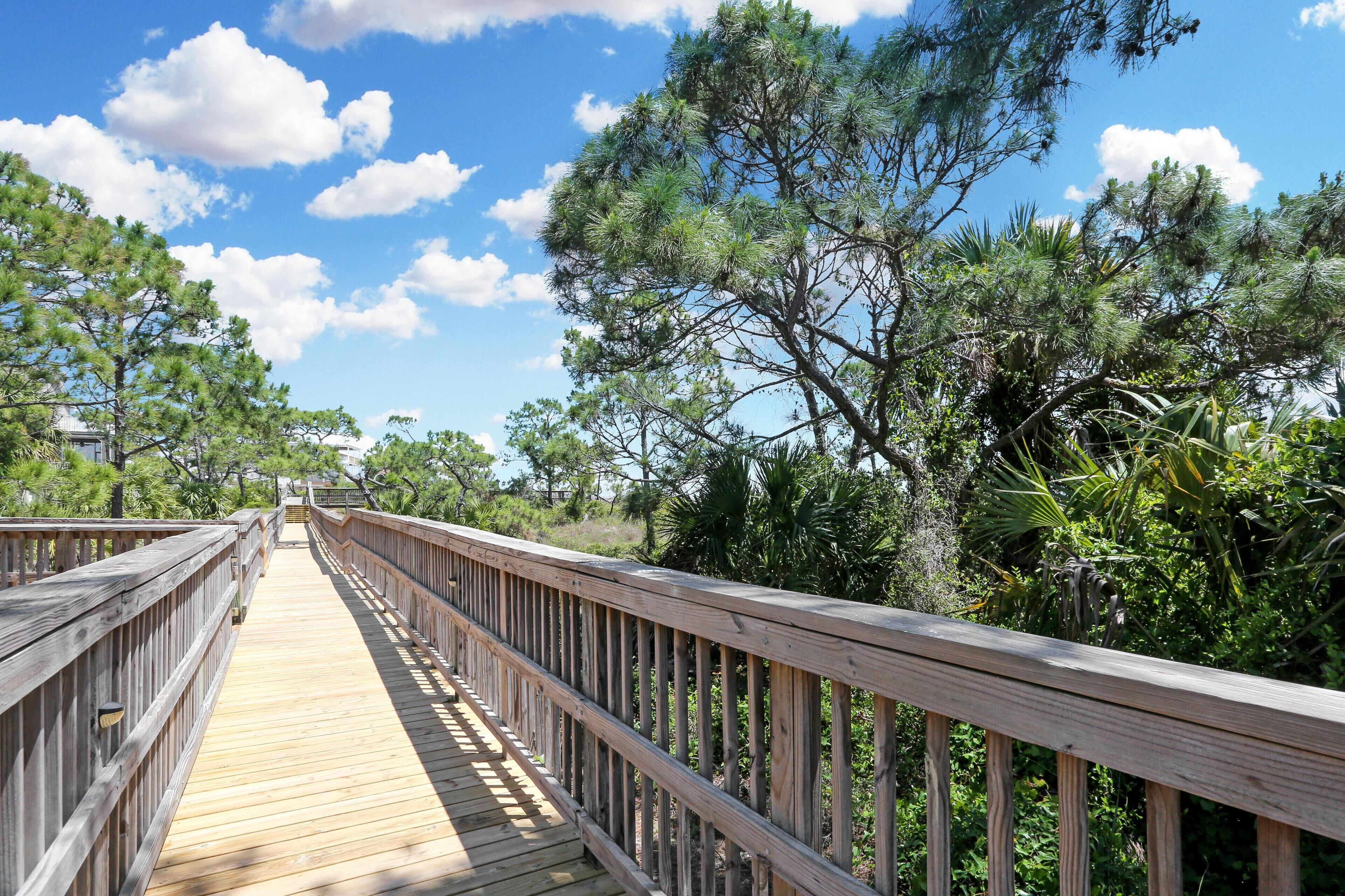 A wooden boardwalk leading through a natural area with trees and a clear sky.
