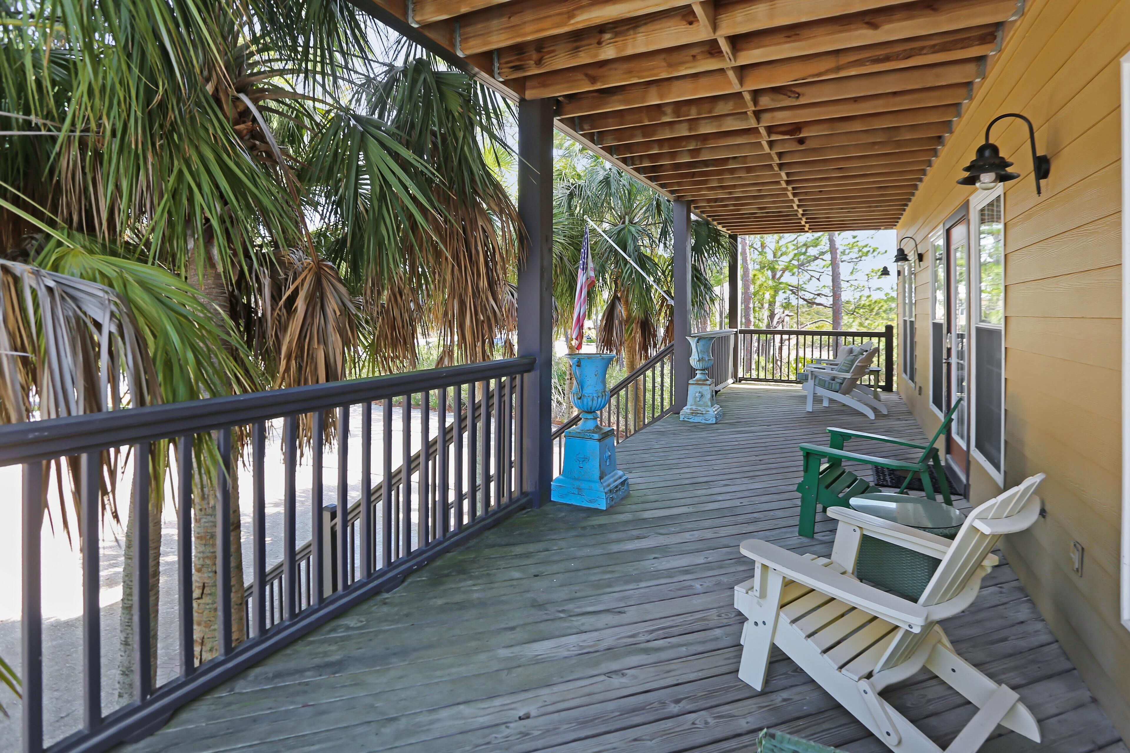 A covered porch with wooden railings, outdoor furniture, and palm trees.