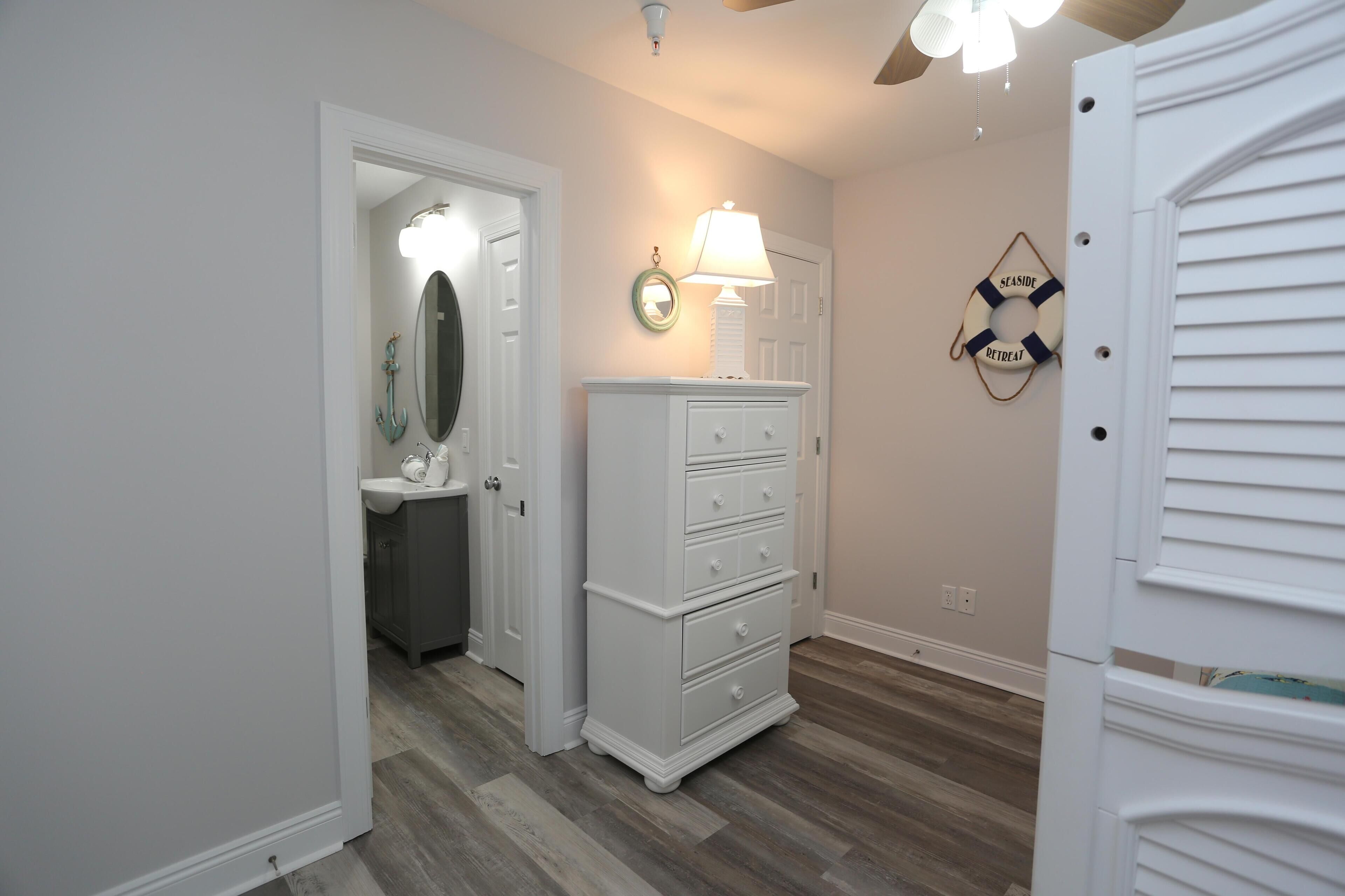 A hallway with a white dresser, a mirror, and a wall-mounted lamp.