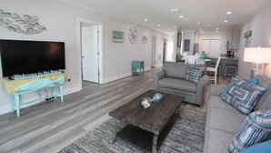 A spacious living room with a gray sofa, a wooden coffee table, and a television on a stand. - Beach Destiny (Port St. Joe)