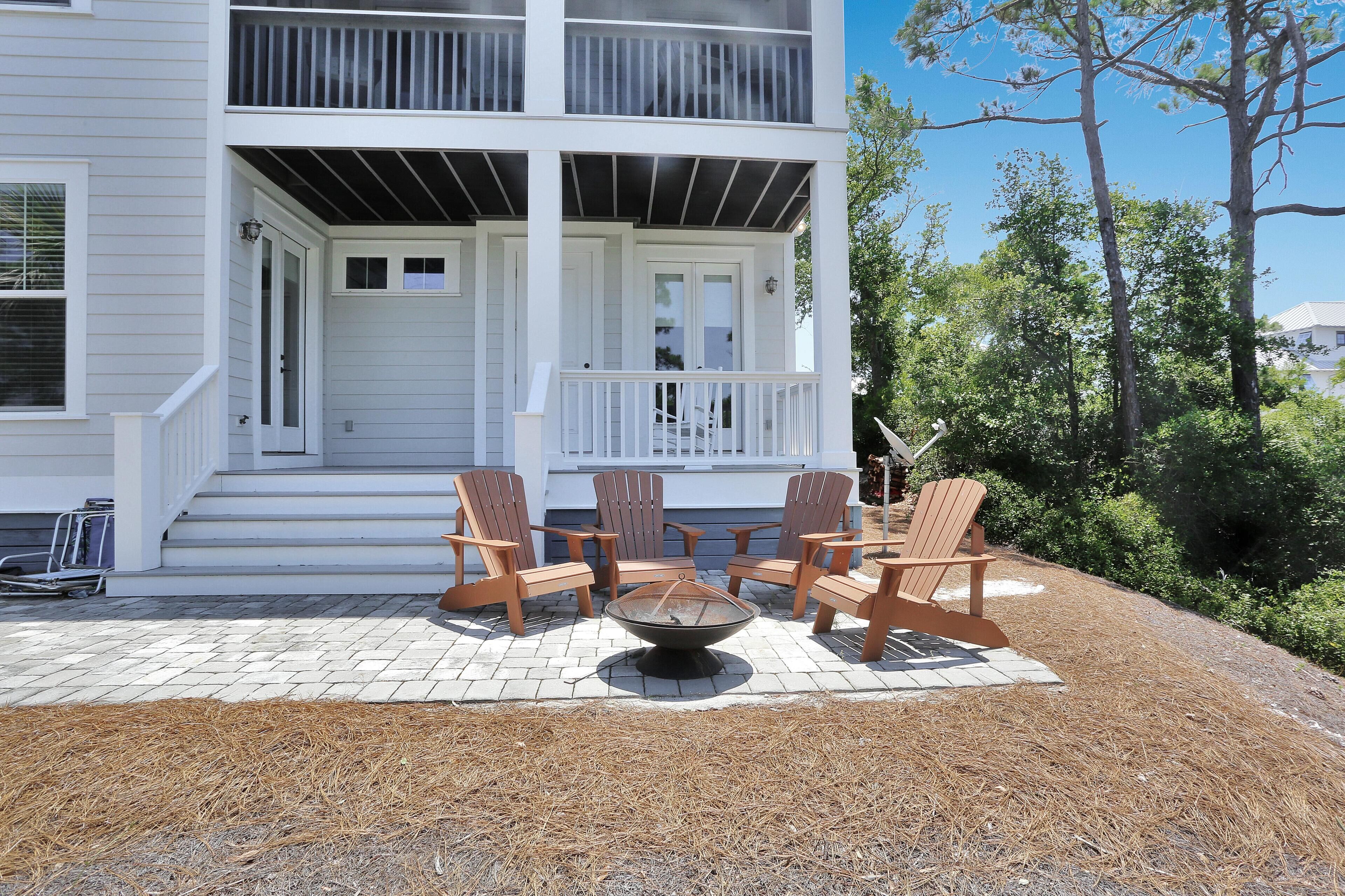 A two-story house with a covered porch, outdoor seating area with Adirondack chairs, and a fire pit.