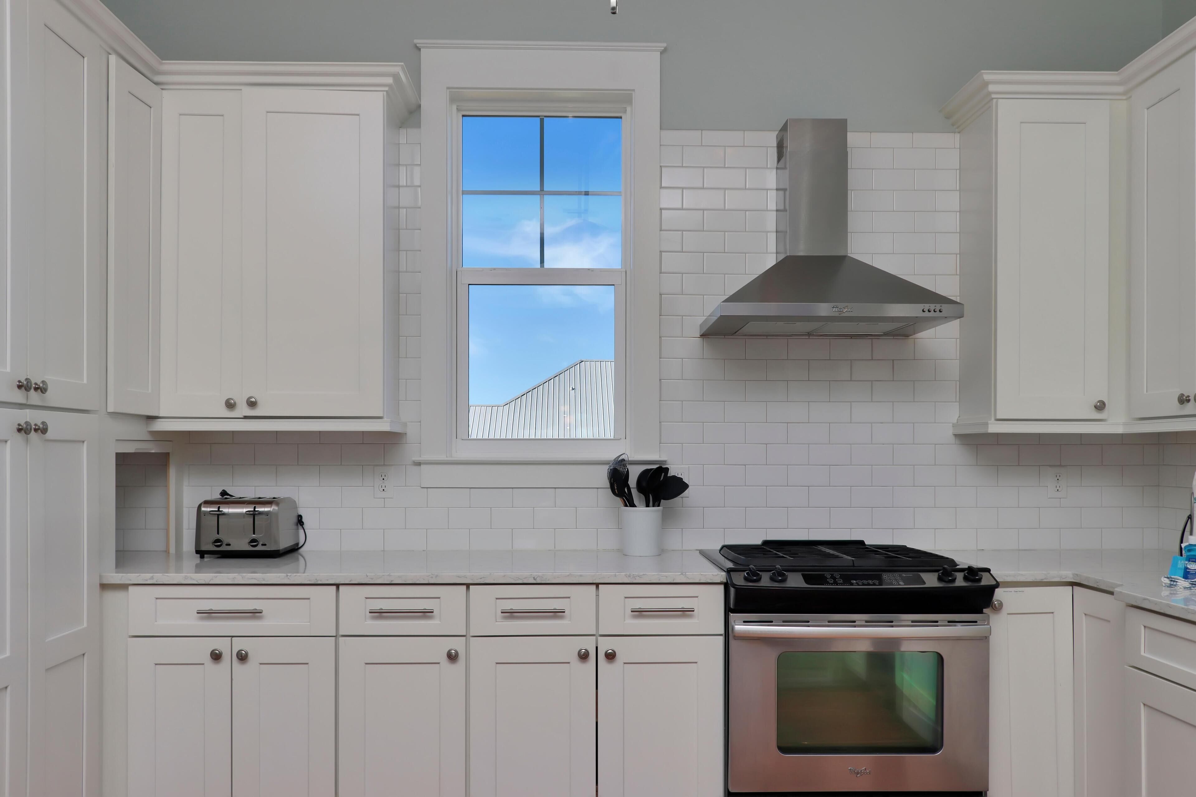 A kitchen with white cabinets, a toaster, a stove, and a window with a view of a building.