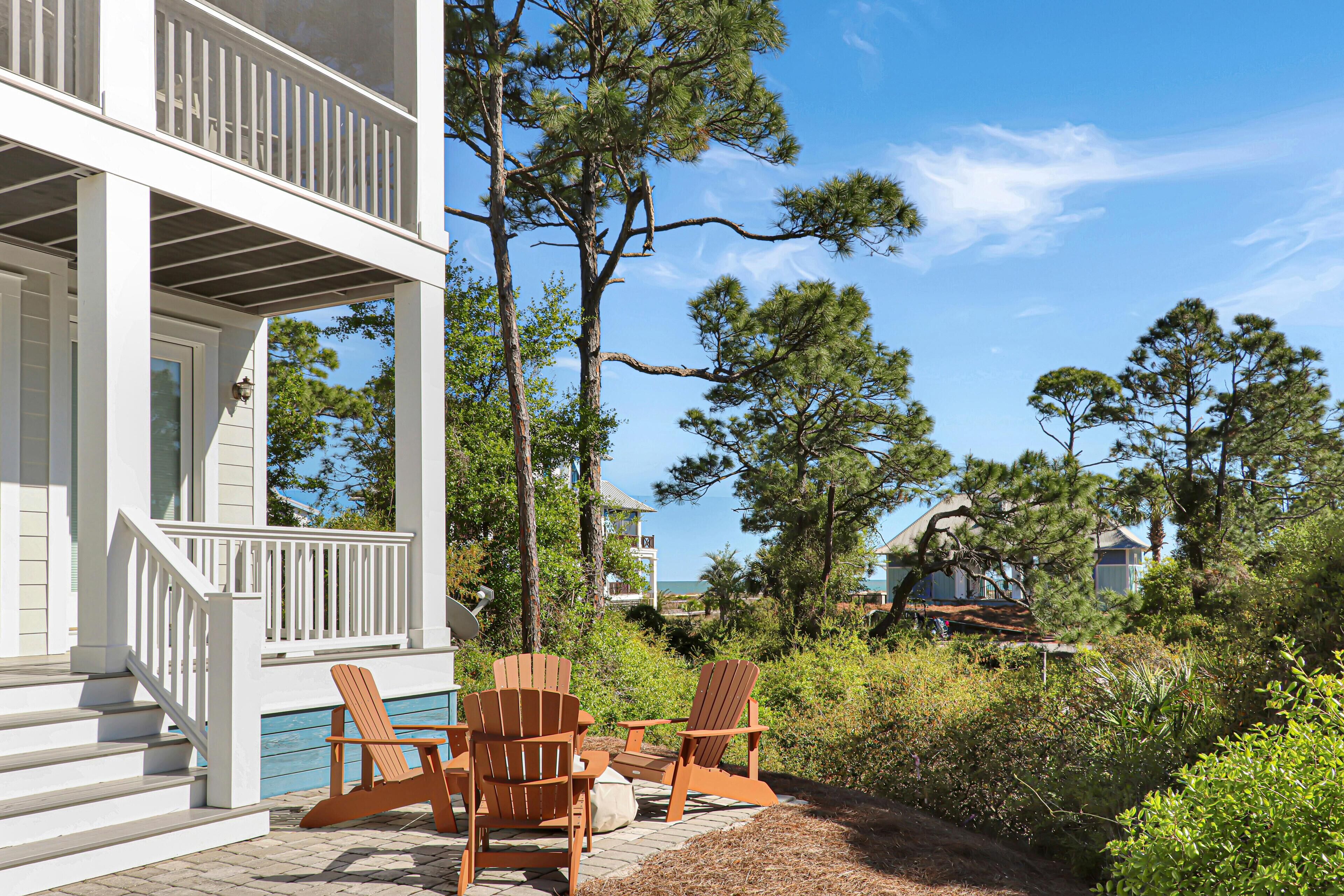 A wooden deck with Adirondack chairs, a pool, and a view of the ocean and surrounding trees.