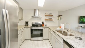 A modern kitchen with white cabinets, stainless steel appliances, and a granite countertop. - Buckeye Beach House (Port St. Joe)
