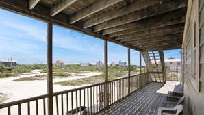 A covered outdoor area with a wooden deck, metal railing, and a view of the beach and buildings in the distance. - Buckeye Beach House (Port St. Joe)