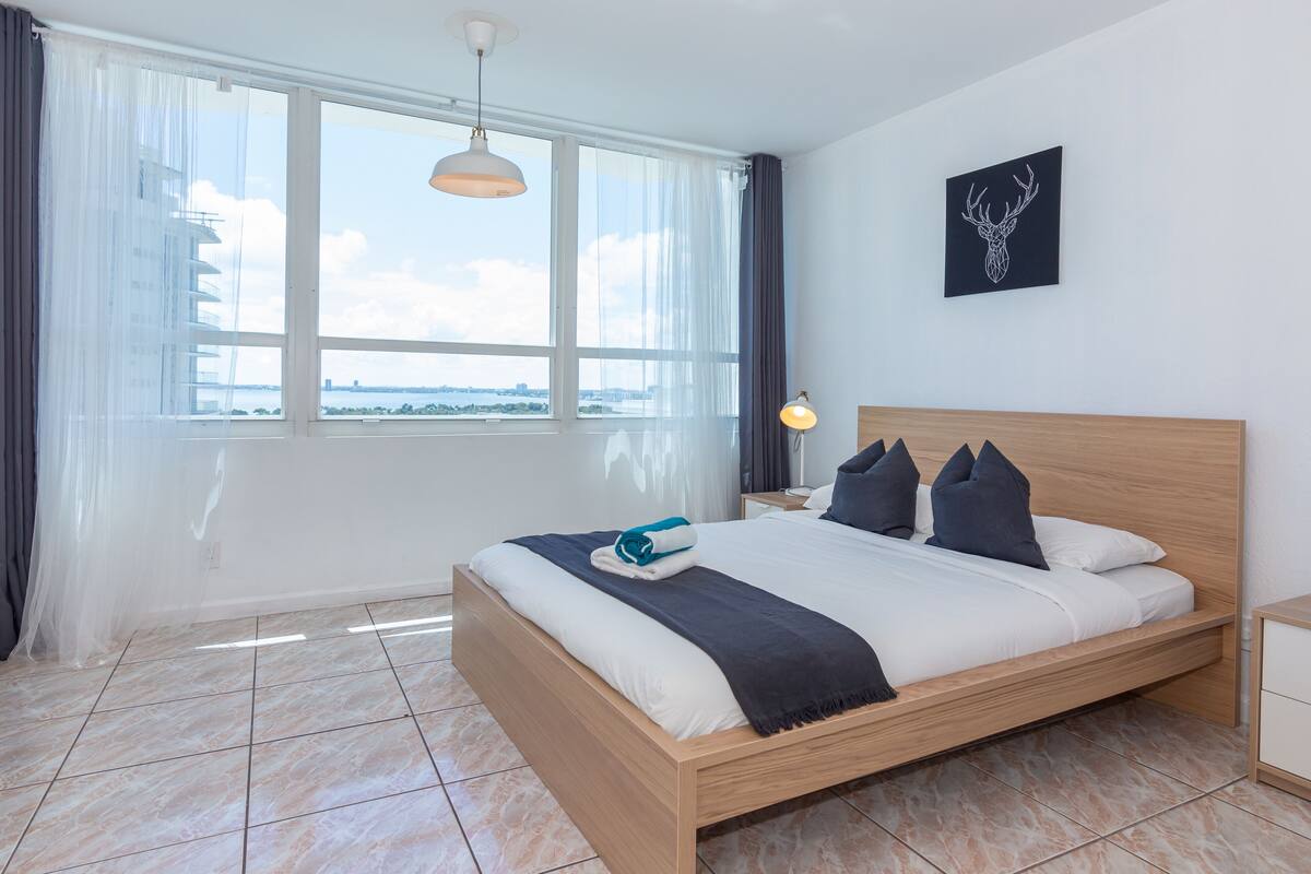Quarto de hotel moderno com uma cama grande, vista para a cidade e decoração simples.