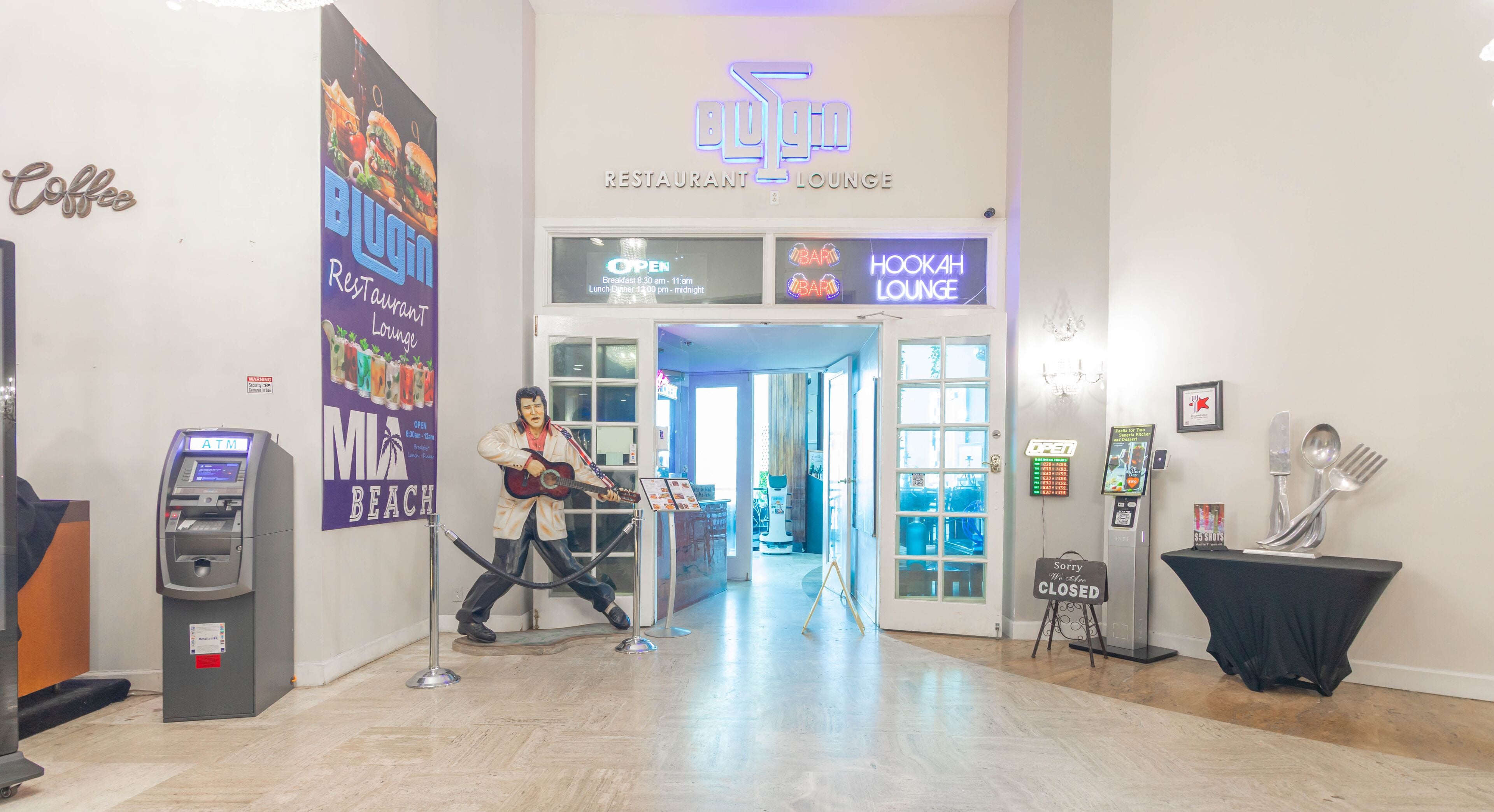 A lobby with a neon sign for a restaurant lounge, an ATM, and a statue of a musician.