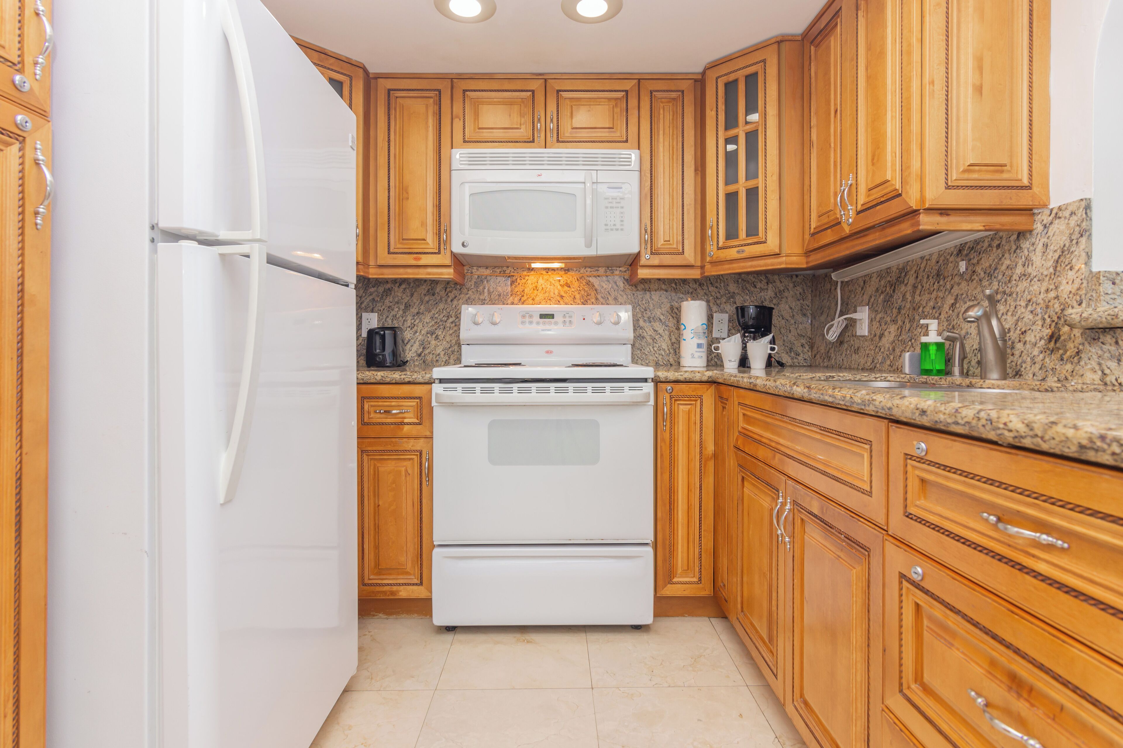 A kitchen with wooden cabinets, a white refrigerator, a microwave, and a stove.