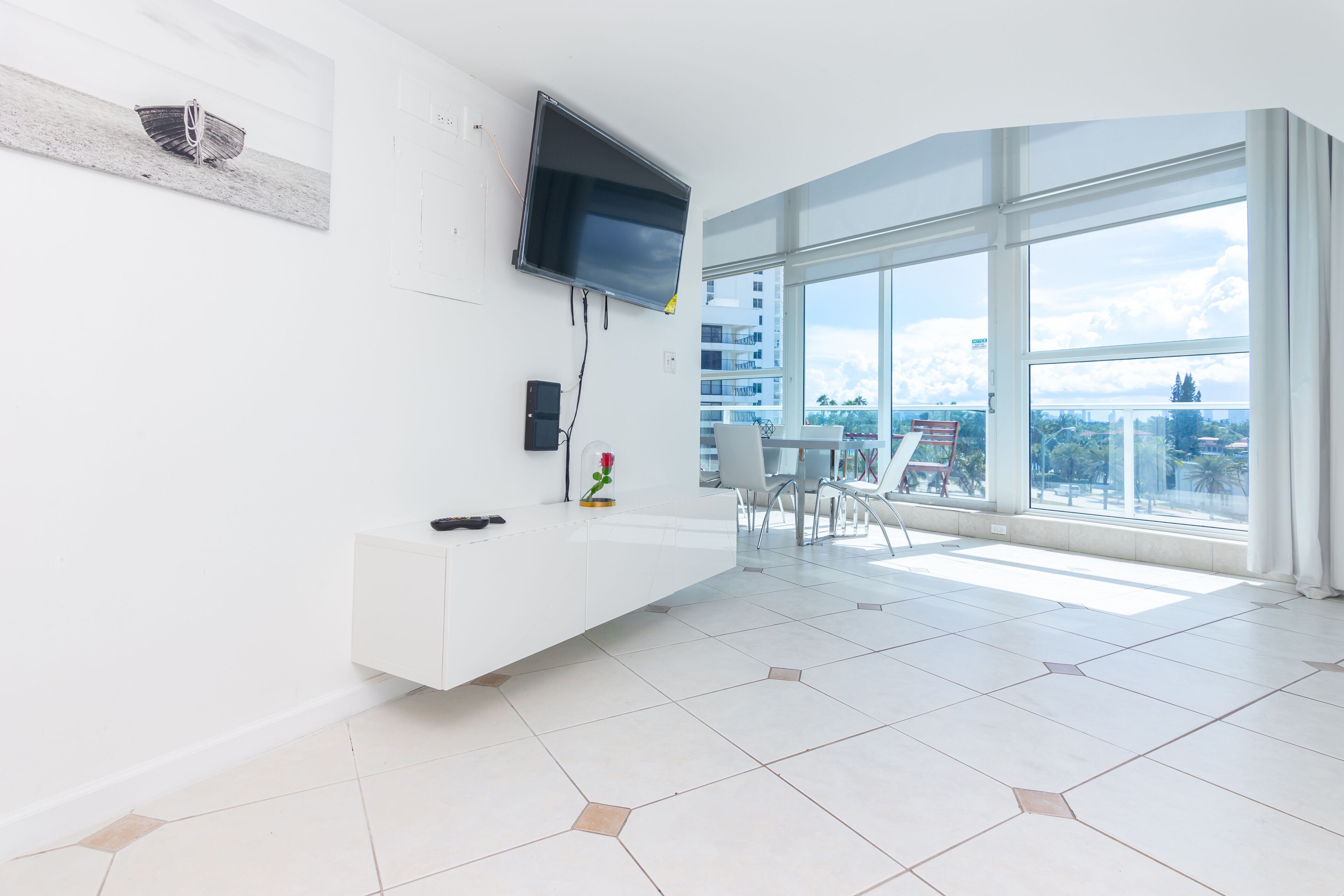 Un salon moderne doté d’une grande fenêtre, d’un téléviseur à écran plat fixé au mur et d’une console blanche au design épuré.