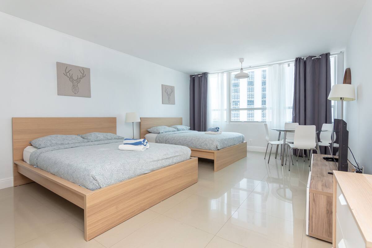 Quarto de hotel moderno com duas camas de madeira, uma escrivaninha e uma cadeira.