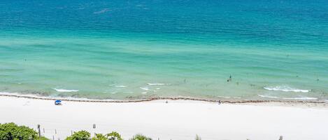 A beach with clear turquoise water, a sandy shore, and palm trees.