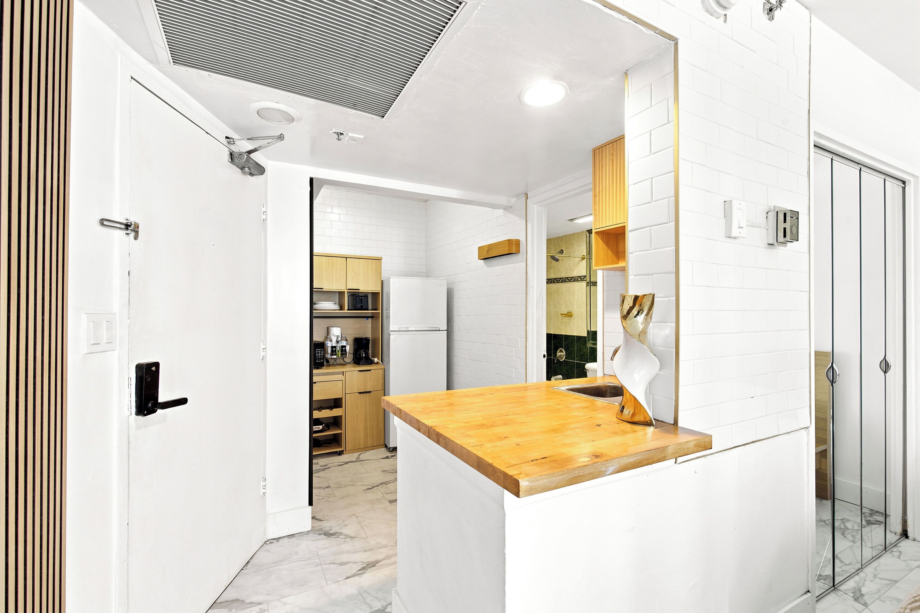 A modern kitchen with white cabinetry, a wooden countertop, and a glass-enclosed shower area.