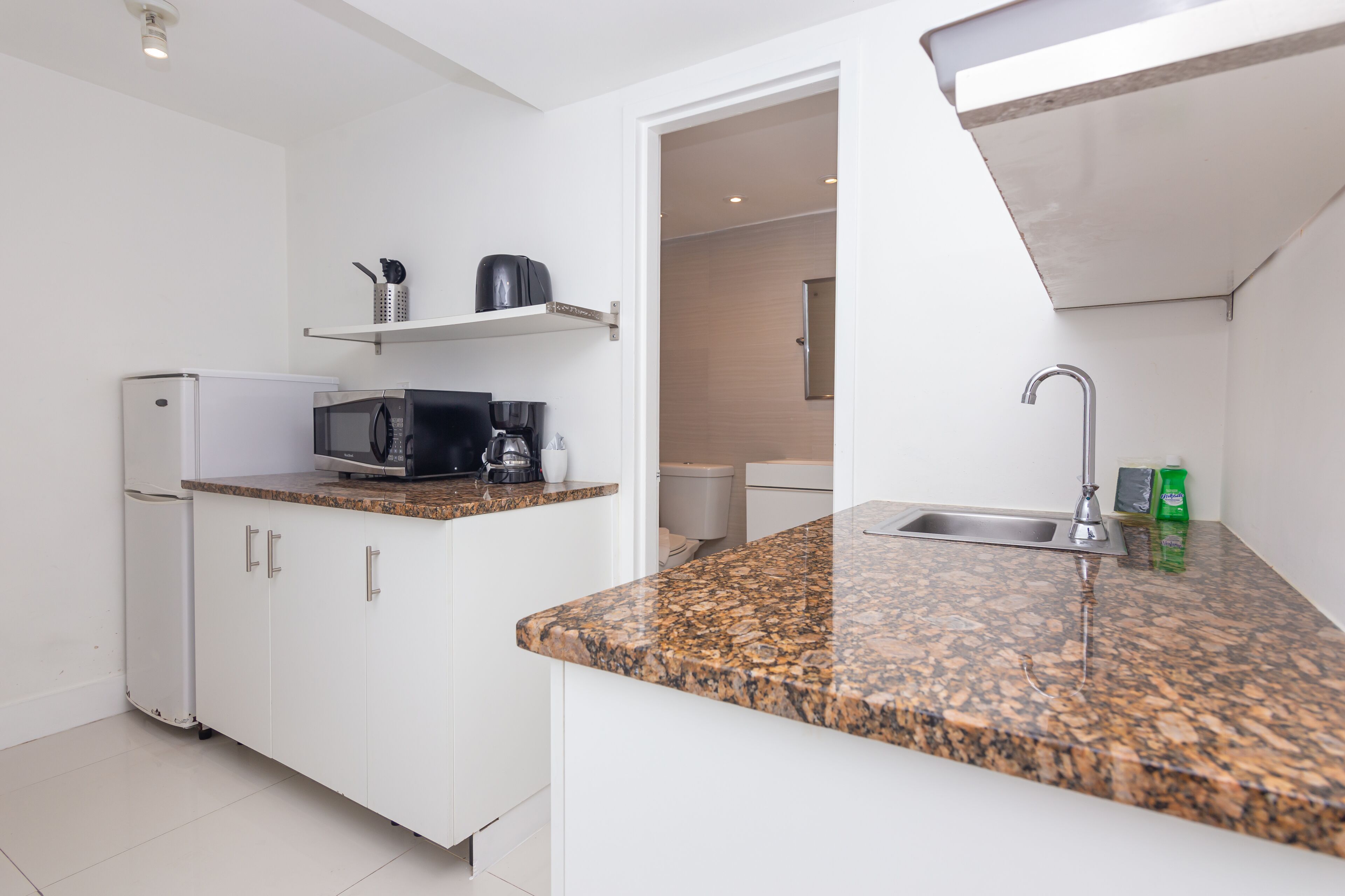 Una cocina moderna con armarios blancos, encimera de granito, microondas integrado, cafetera y un lavabo.