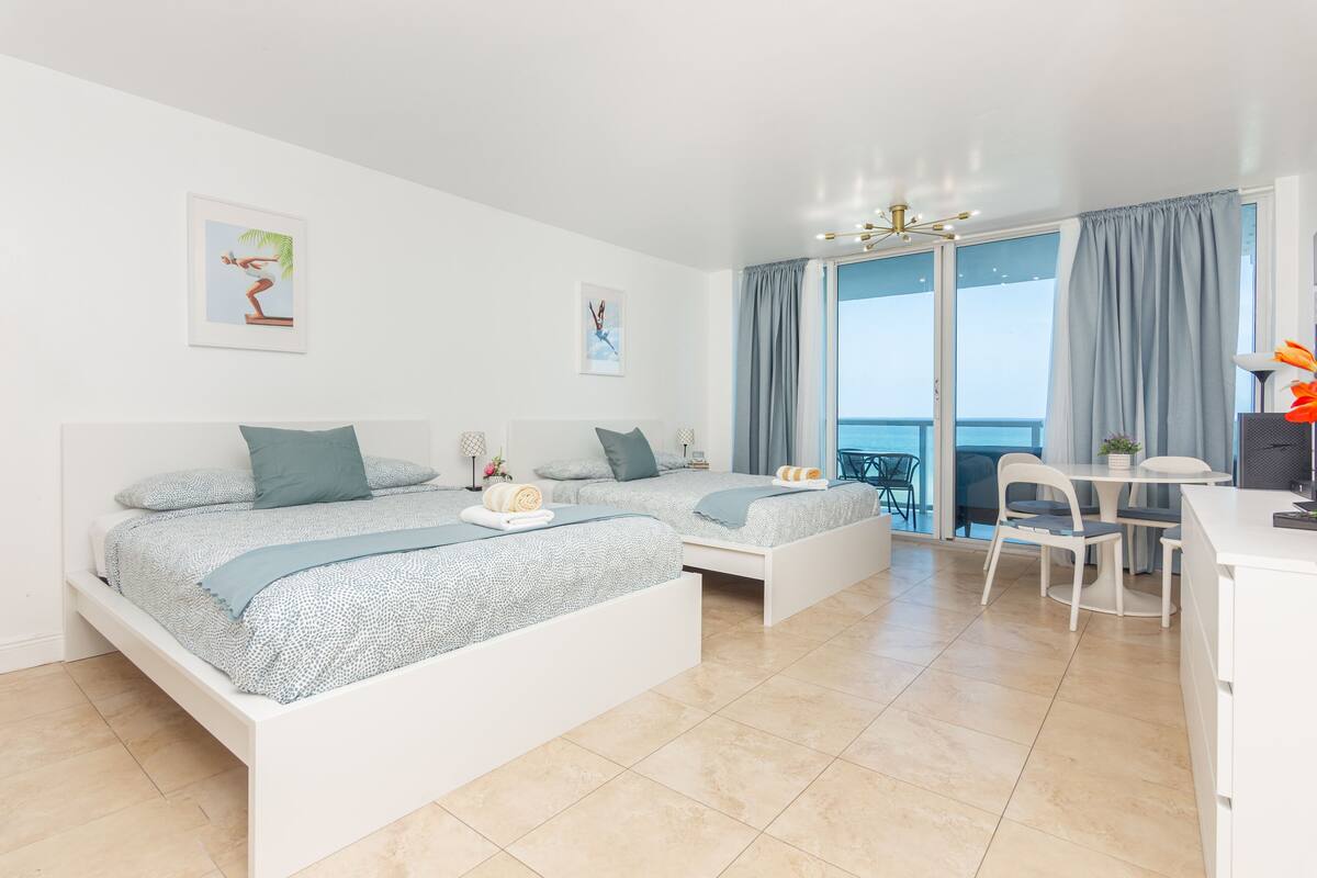 Quarto moderno com duas camas, varanda e área de refeições.