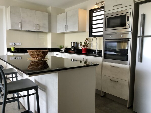 A modern kitchen with white cabinets, a black countertop, stainless steel appliances, and a central island with bar stools.