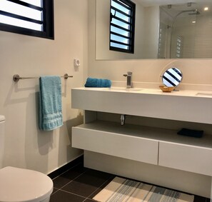 A modern bathroom with a white sink, a mirror, a towel rack, and a toilet.
