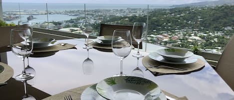 A dining table set with plates, glasses, and cutlery, overlooking a scenic view of a coastal city.