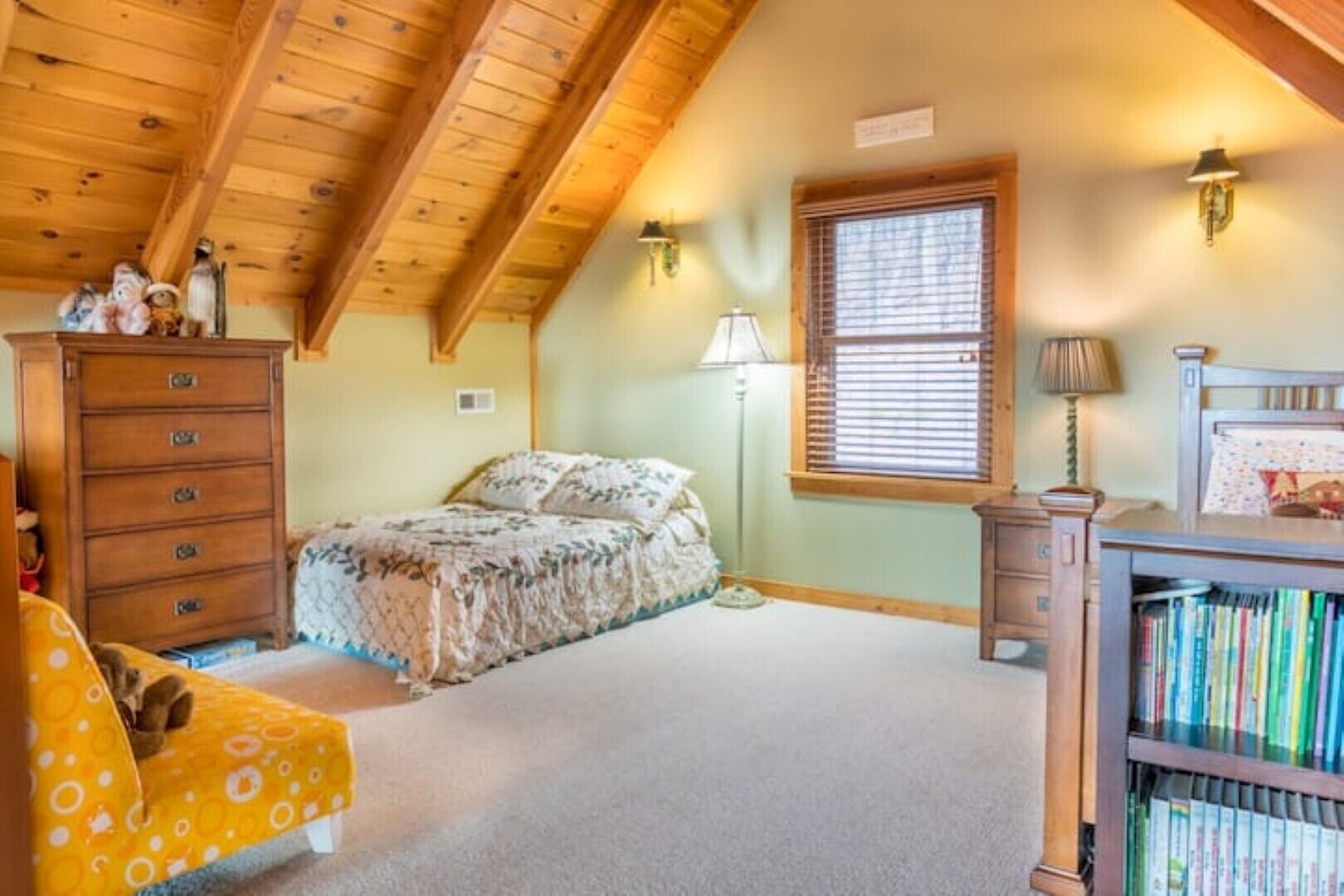 Une chambre à coucher avec un lit, une commode, une lampe et une bibliothèque.