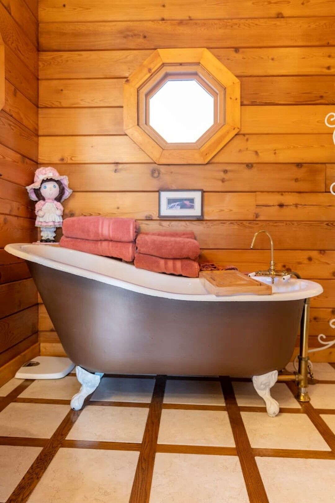A wooden cabin interior with a bathtub, towels, a small figurine, and a framed picture on the wall.