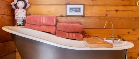 A wooden cabin interior with a bathtub, towels, a small figurine, and a framed picture on the wall.