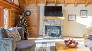 A cozy living room with a stone fireplace, a Christmas tree, and a television mounted above it. - A Sauratown Mountain Getaway (Pinnacle)