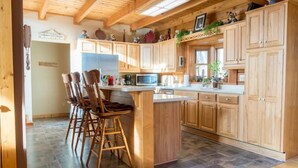A kitchen with wooden cabinets, a central island with bar stools, a refrigerator, and a microwave. - A Sauratown Mountain Getaway (Pinnacle)