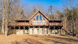 A cabin with a wooden deck, a large window, and a staircase leading to a second level. - A Sauratown Mountain Getaway (Pinnacle)