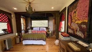 Un dormitorio acogedor con suelo de madera, una cama con manta colorida, un escritorio con máquina de escribir y un cuadro grande en la pared.