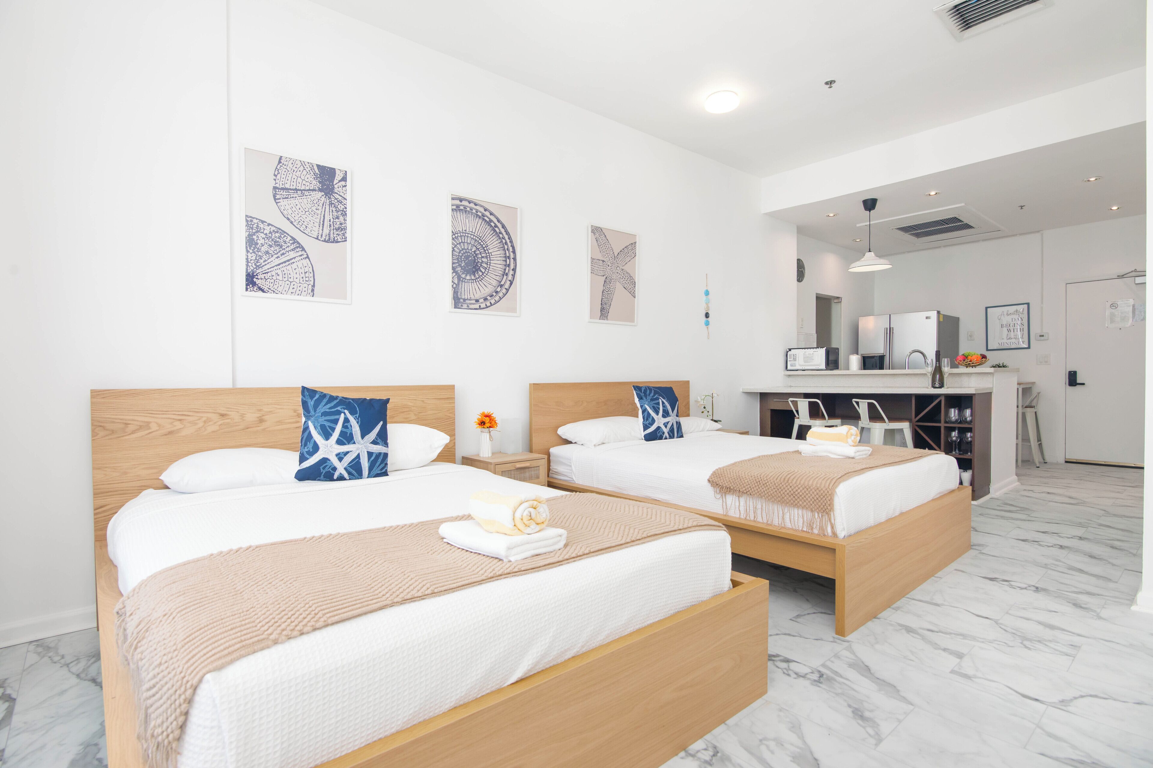 A hotel room with two beds, a desk, and a kitchenette.