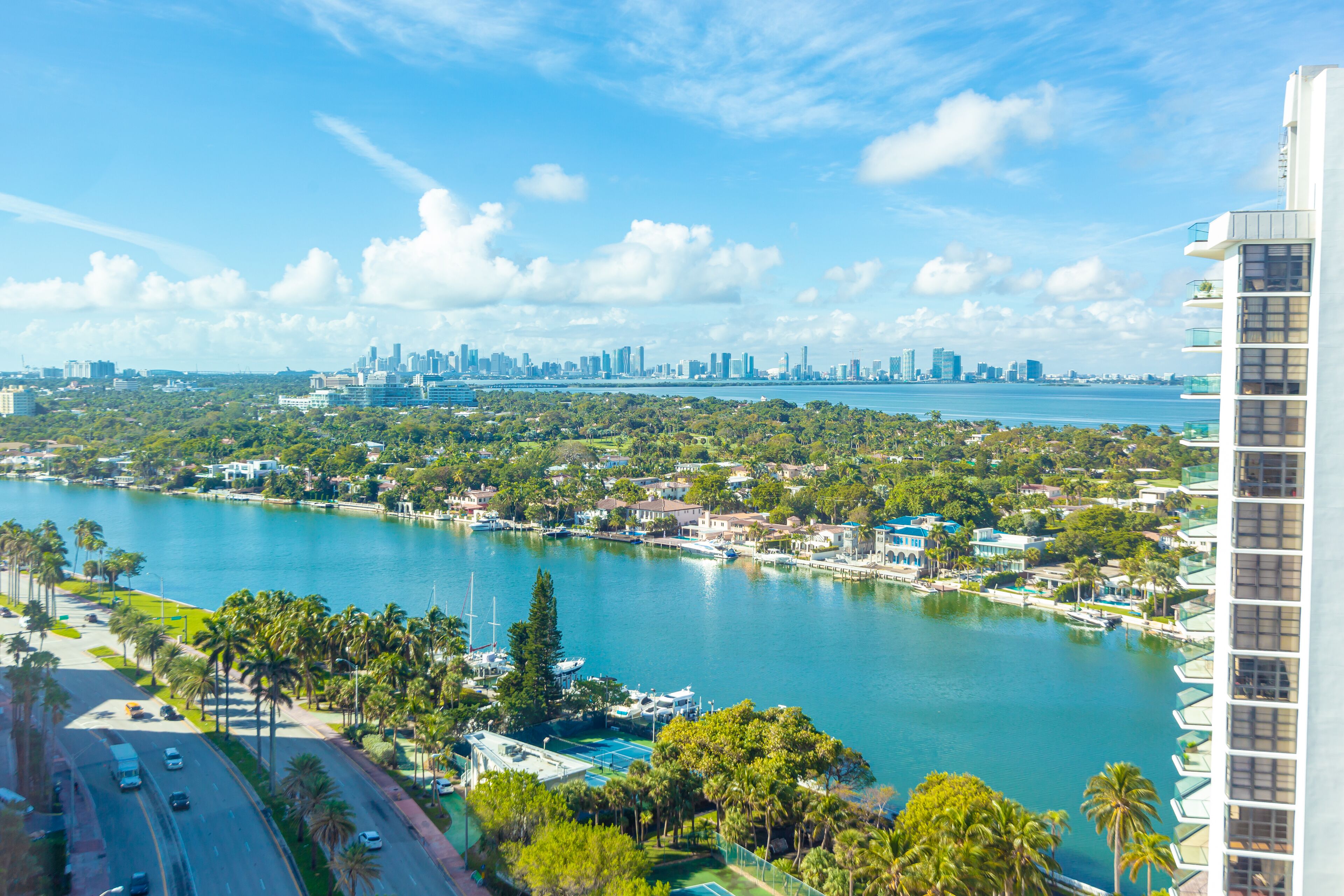 A high-rise hotel overlooking a marina with boats, a city skyline in the distance, and a clear blue sky.