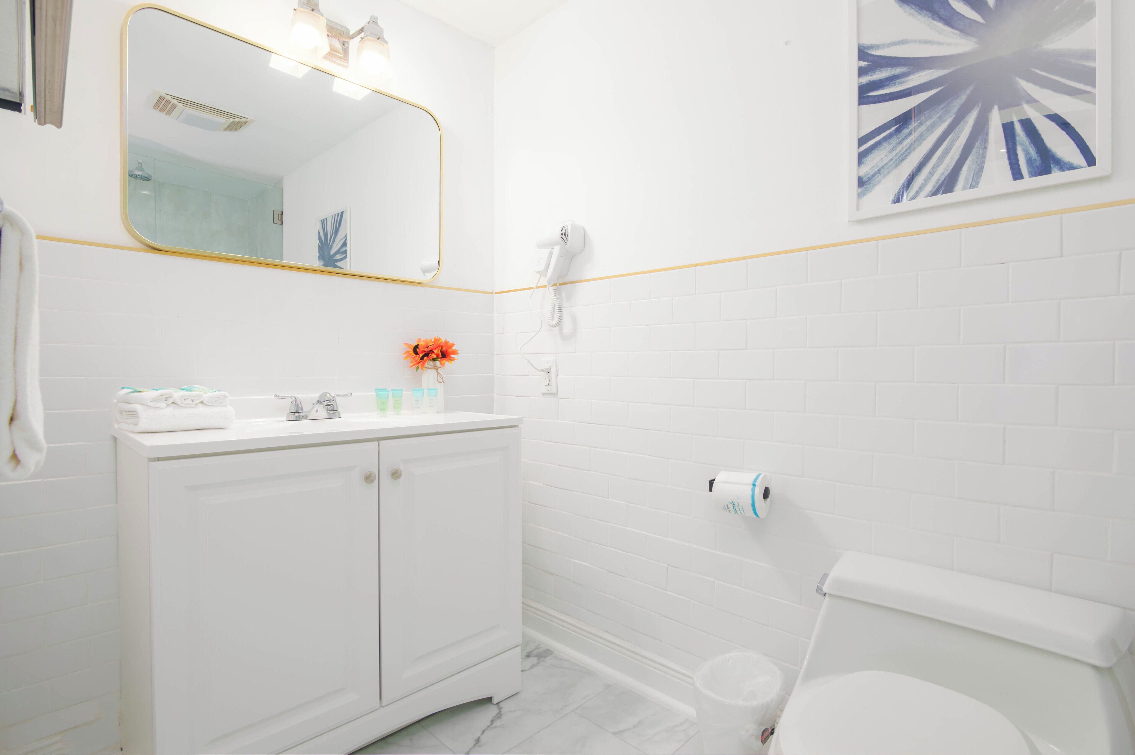 A modern bathroom with a white vanity, a mirror, a hairdryer, and a toilet.