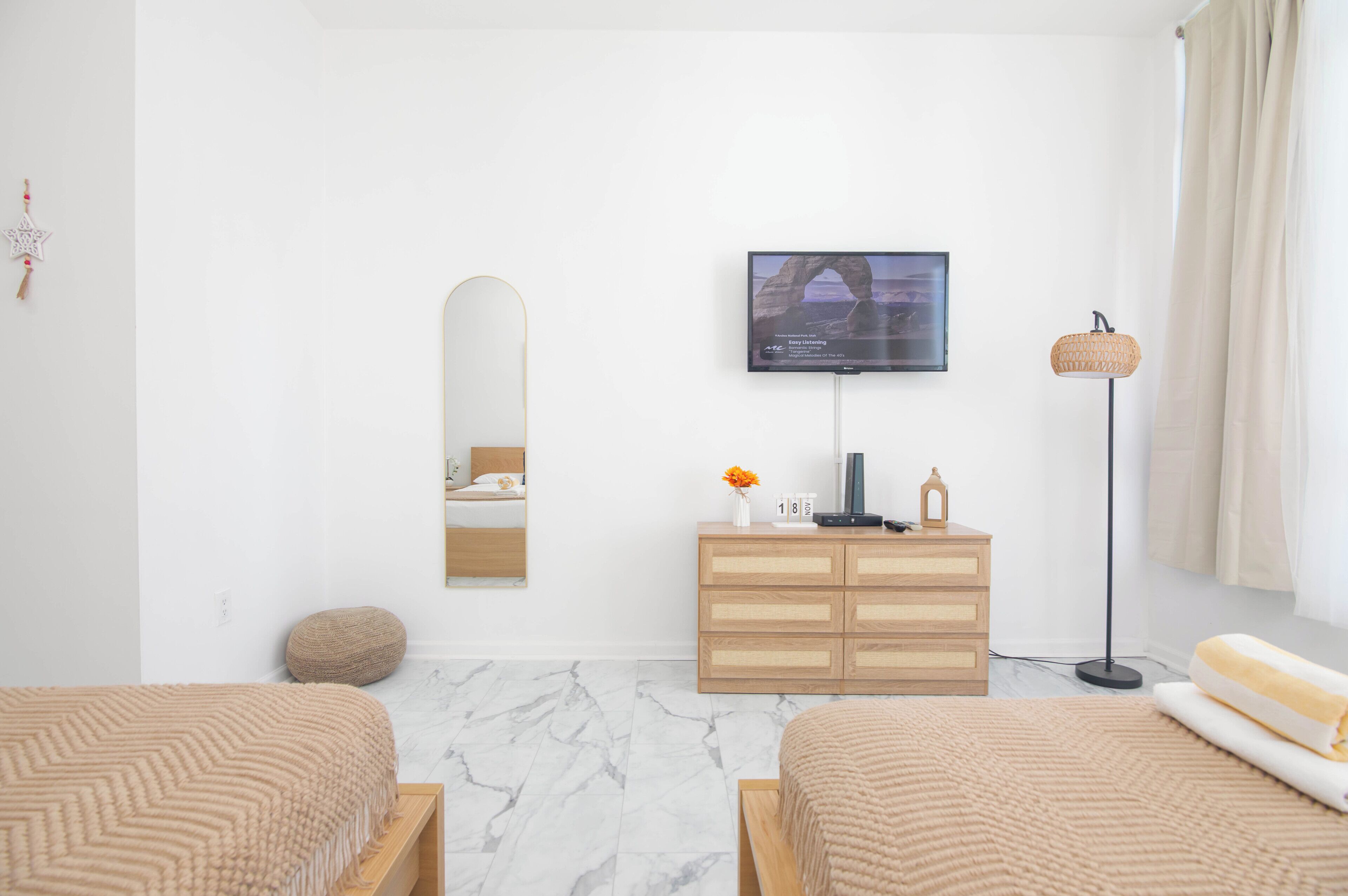 A modern hotel room with a bed, a dresser, a television, and a floor lamp.