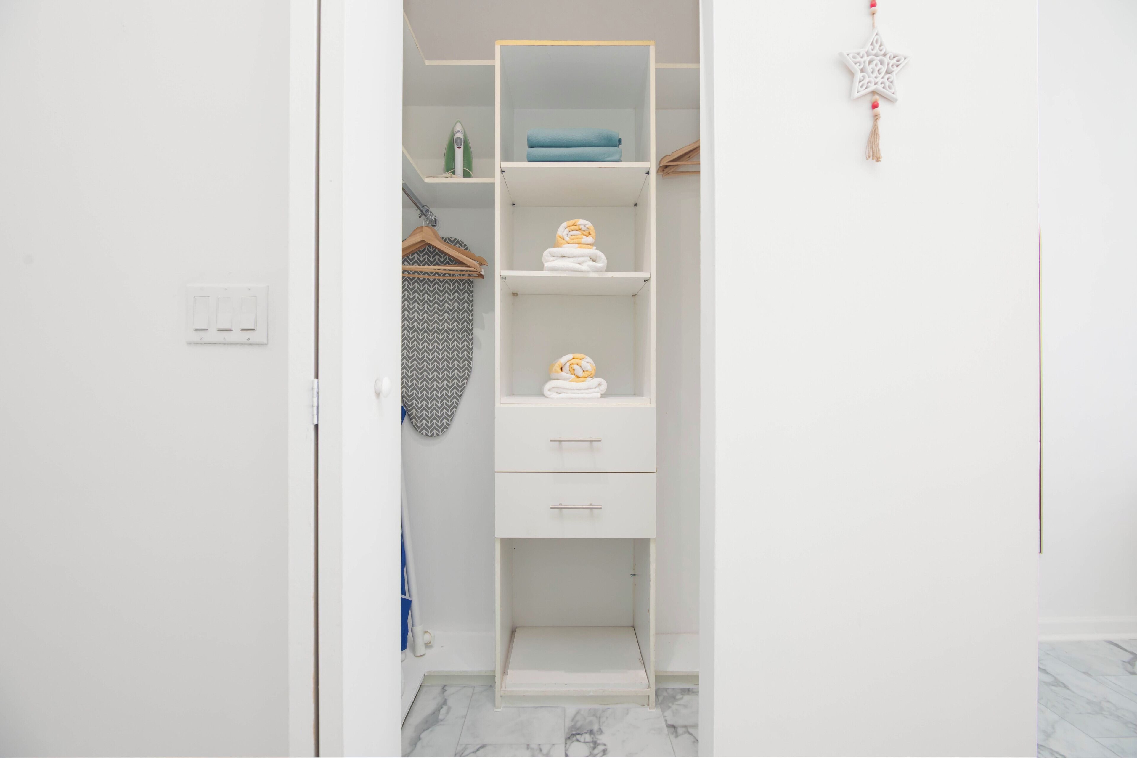 A white walk-in closet with shelves and drawers, a hanging rack, and a star-shaped ornament.