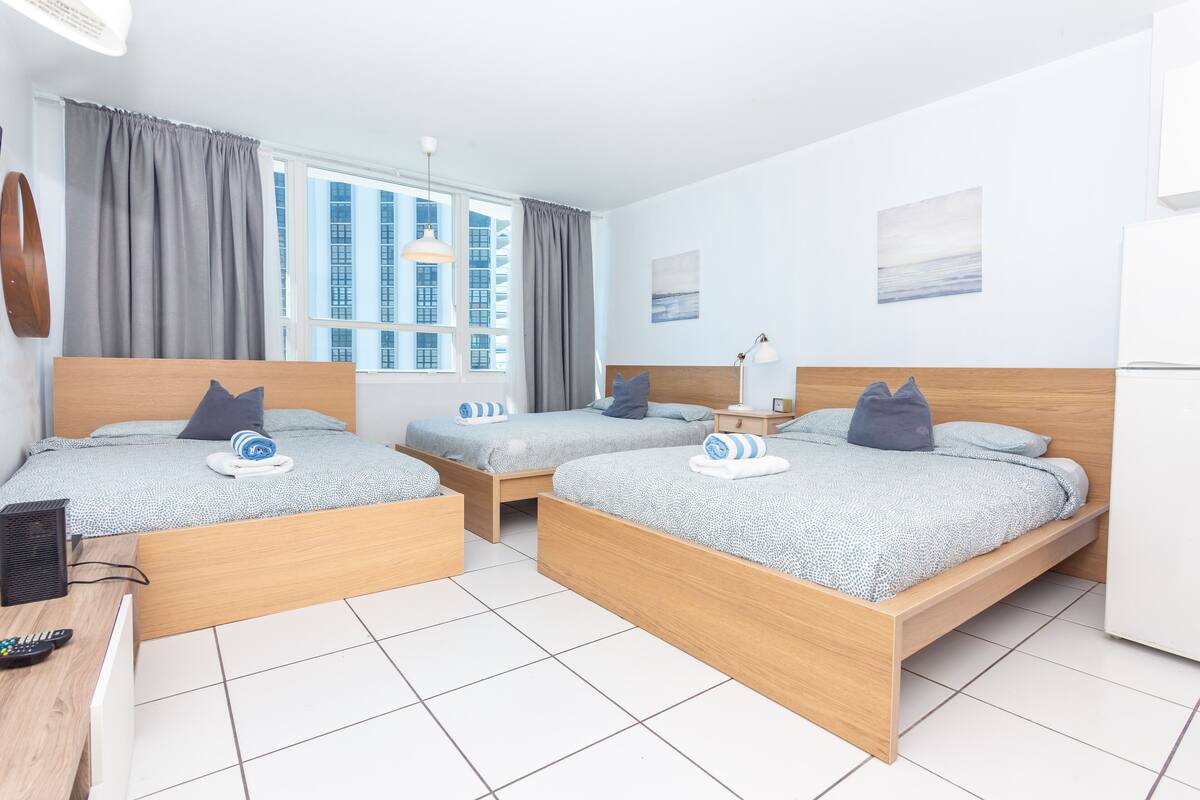 A hotel room with two beds, a desk with a computer, and a window with curtains.