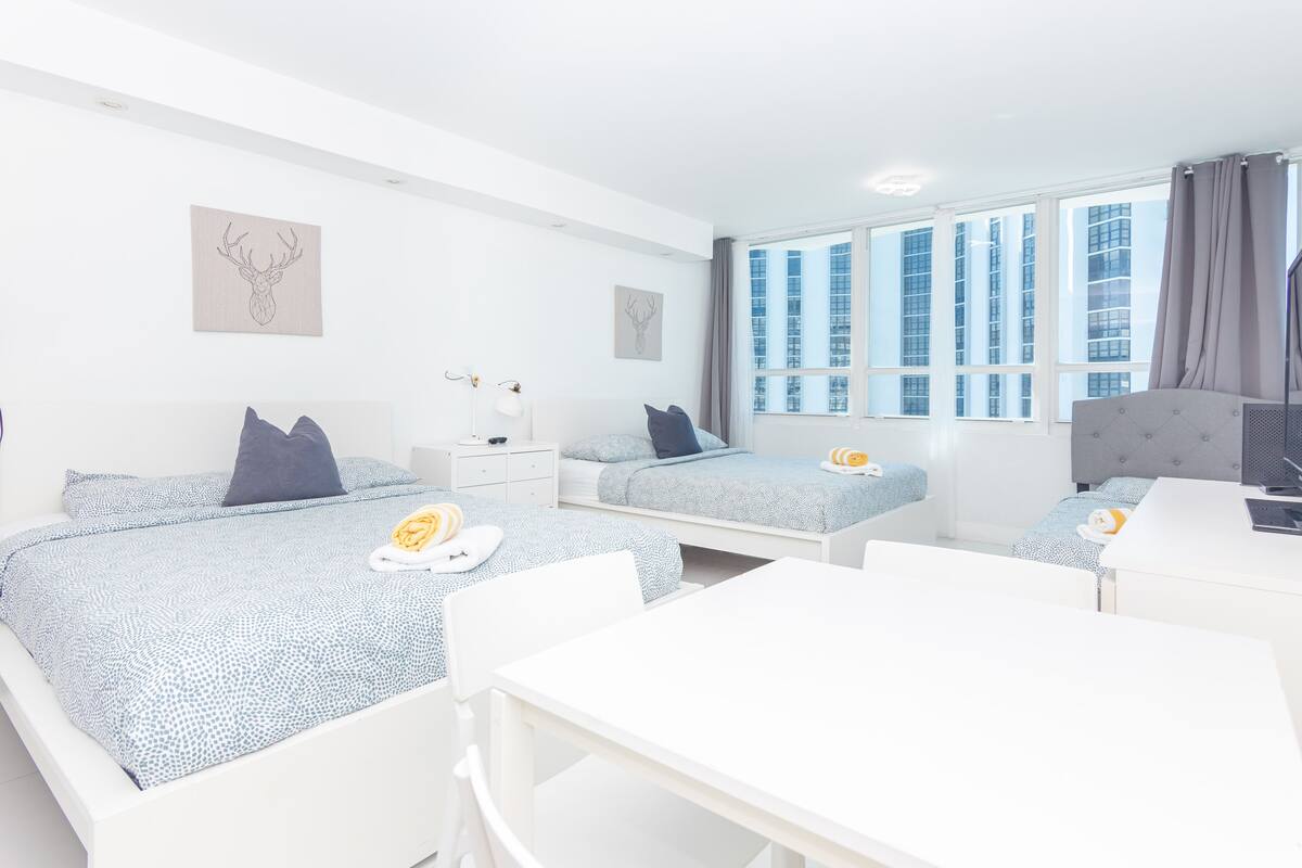A modern hotel room with two beds, a desk, and a large window.